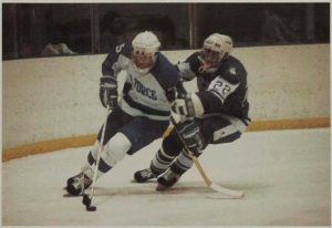 An Air Force player skates with the puck while a Holy Cross defender keeps up with him.