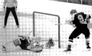 Brown goalie in white sweater sprawls in the crease in front of an Alaska Anchorage player.