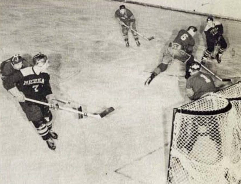 Michigan looks to shoot on net during the first-ever game between Michigan and Denver in 1951. A black and white photo but it appears to be a color-on-color game.